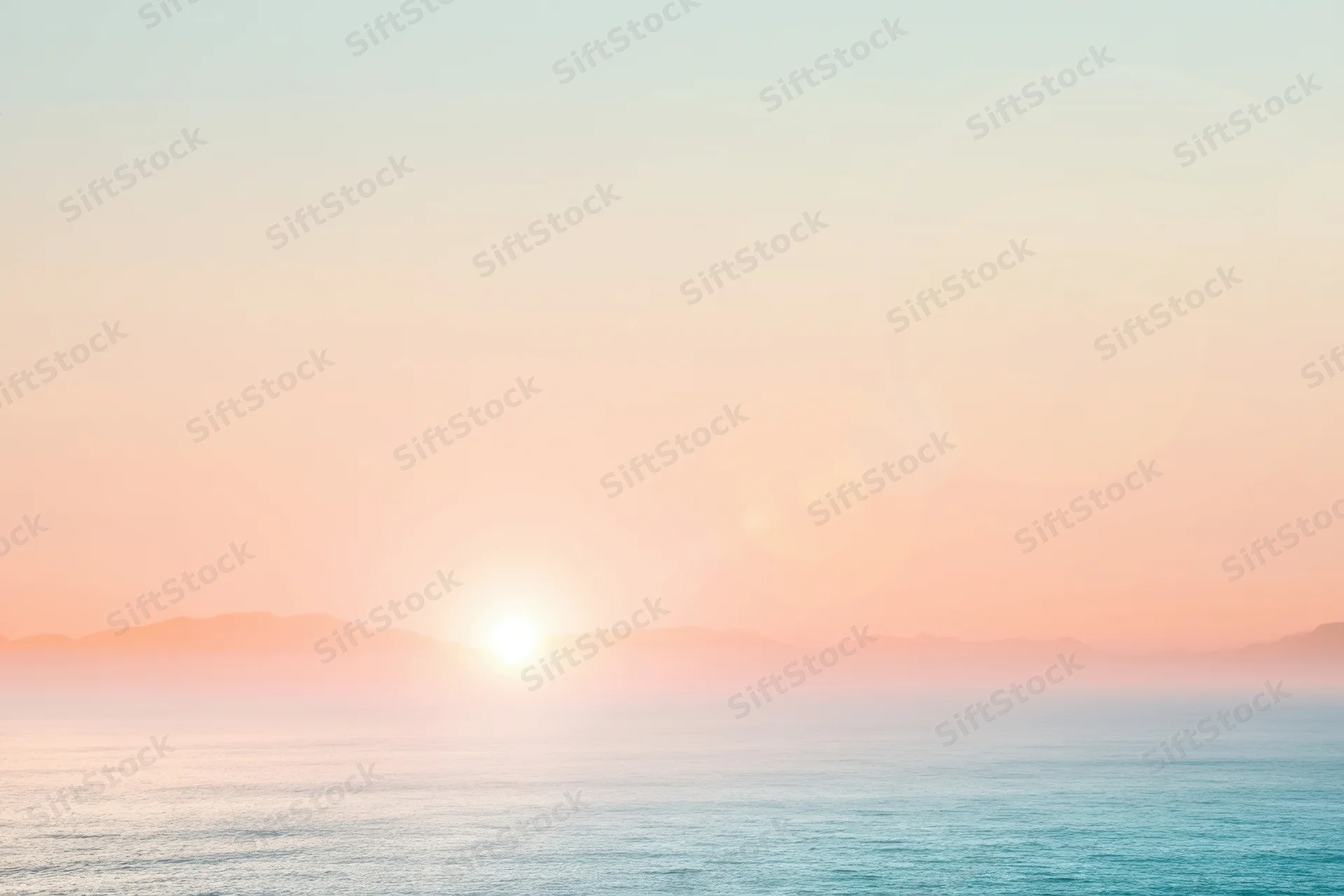Soft sunset over calm ocean with hazy mountains on the horizon