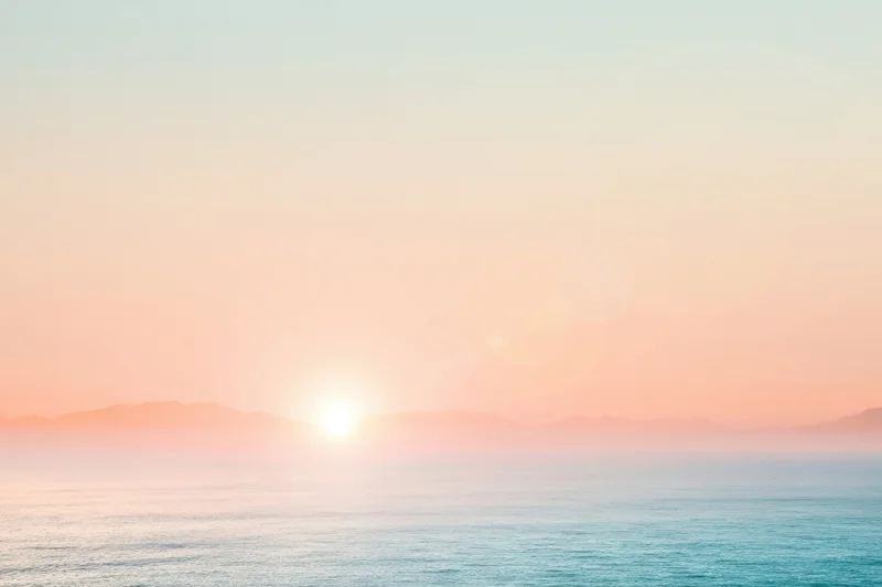 Soft sunset over calm ocean with hazy mountains on the horizon