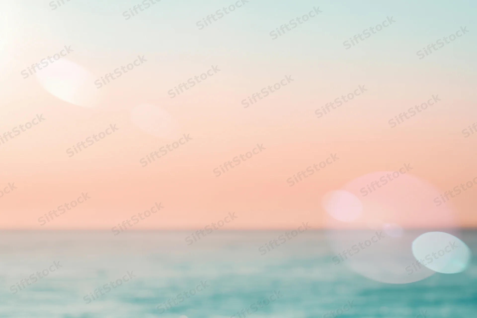 Soft pastel sunset over calm ocean with hazy horizon and bokeh light effects