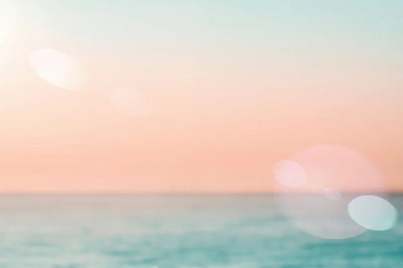 Soft pastel sunset over calm ocean with hazy horizon and bokeh light effects