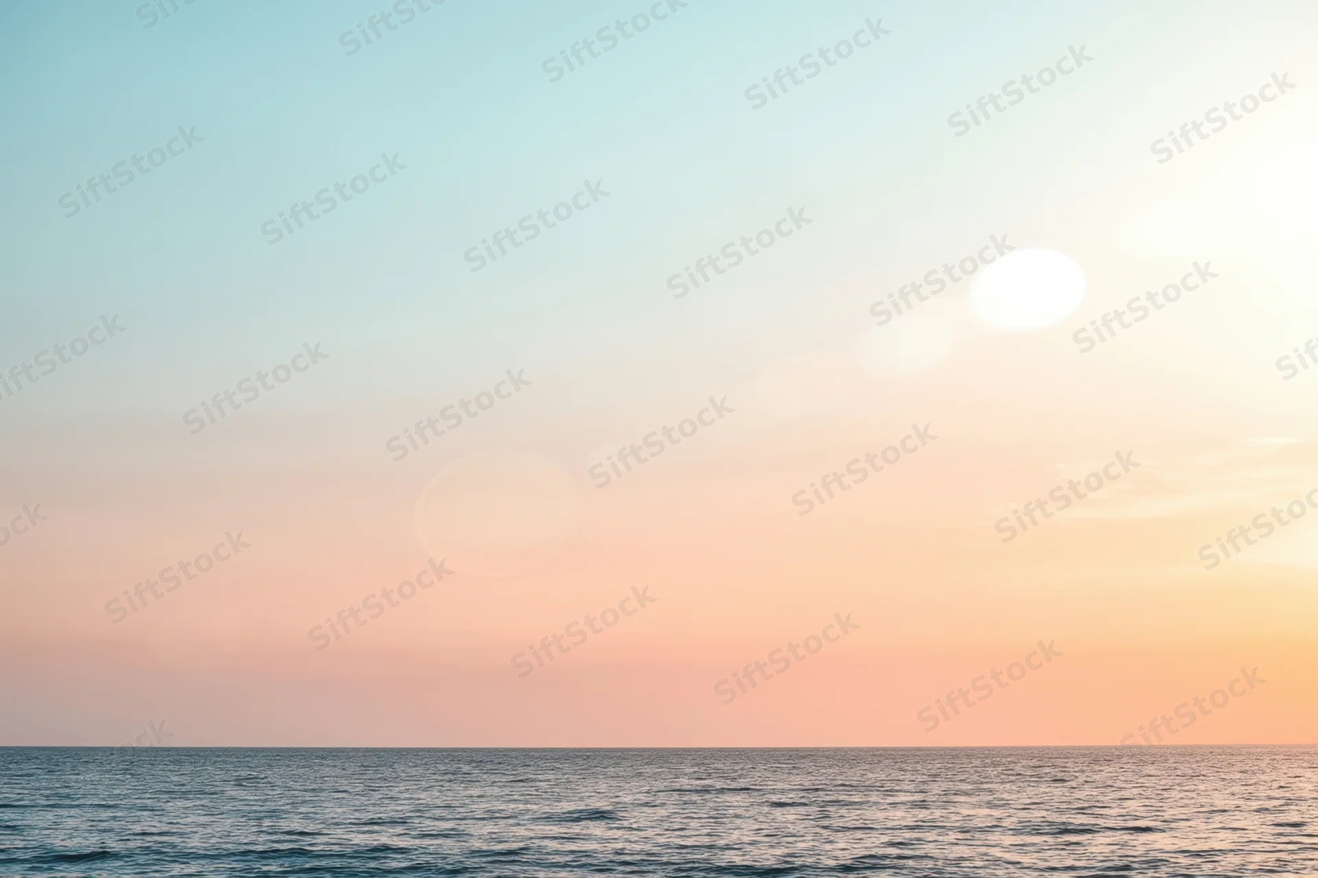 Soft sunlit ocean at sunset with pastel sky and hazy horizon