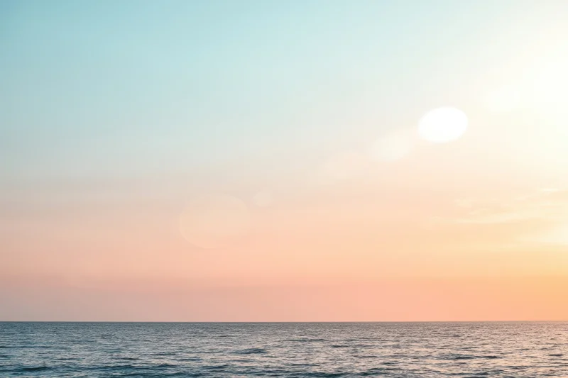 Soft sunlit ocean at sunset with pastel sky and hazy horizon