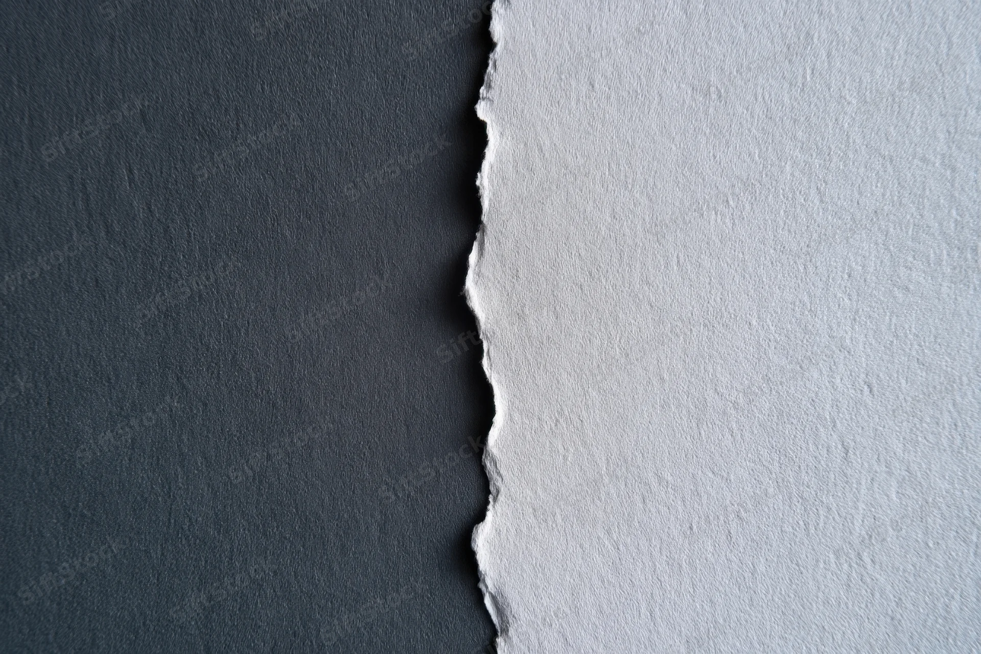 Torn paper edge dividing dark charcoal and light gray textured surfaces