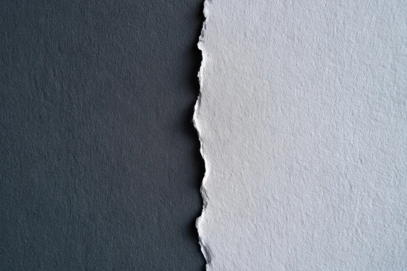 Torn paper edge dividing dark charcoal and light gray textured surfaces