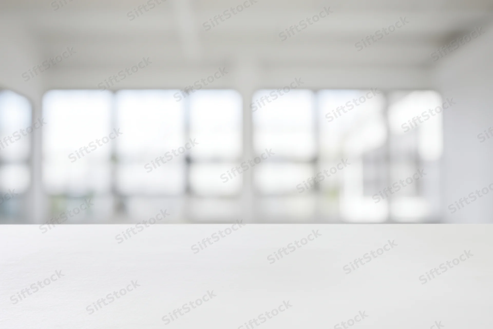 White table in a bright minimalist studio interior with blurred windows in the background
