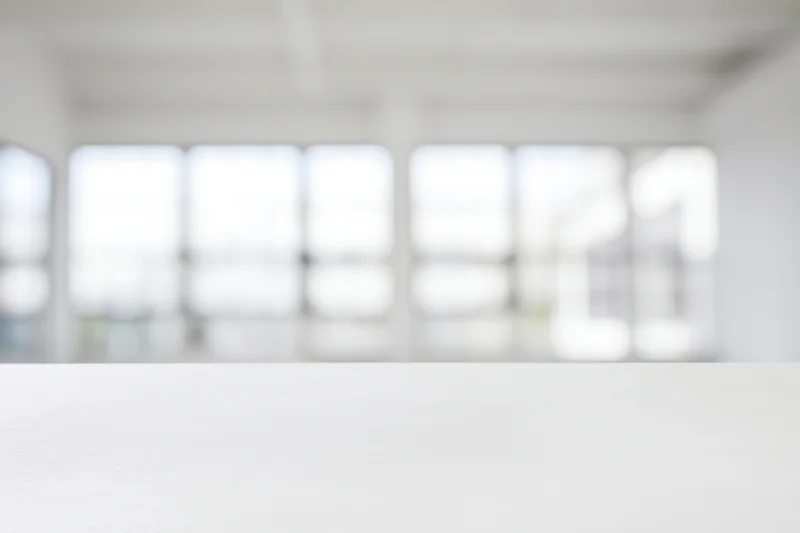 White table in a bright minimalist studio interior with blurred windows in the background
