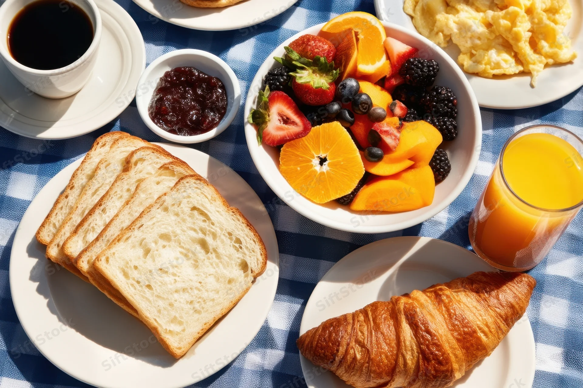 Breakfast spread with fruit, toast, croissant, coffee and juice on a blue checkered tablecloth outdoors