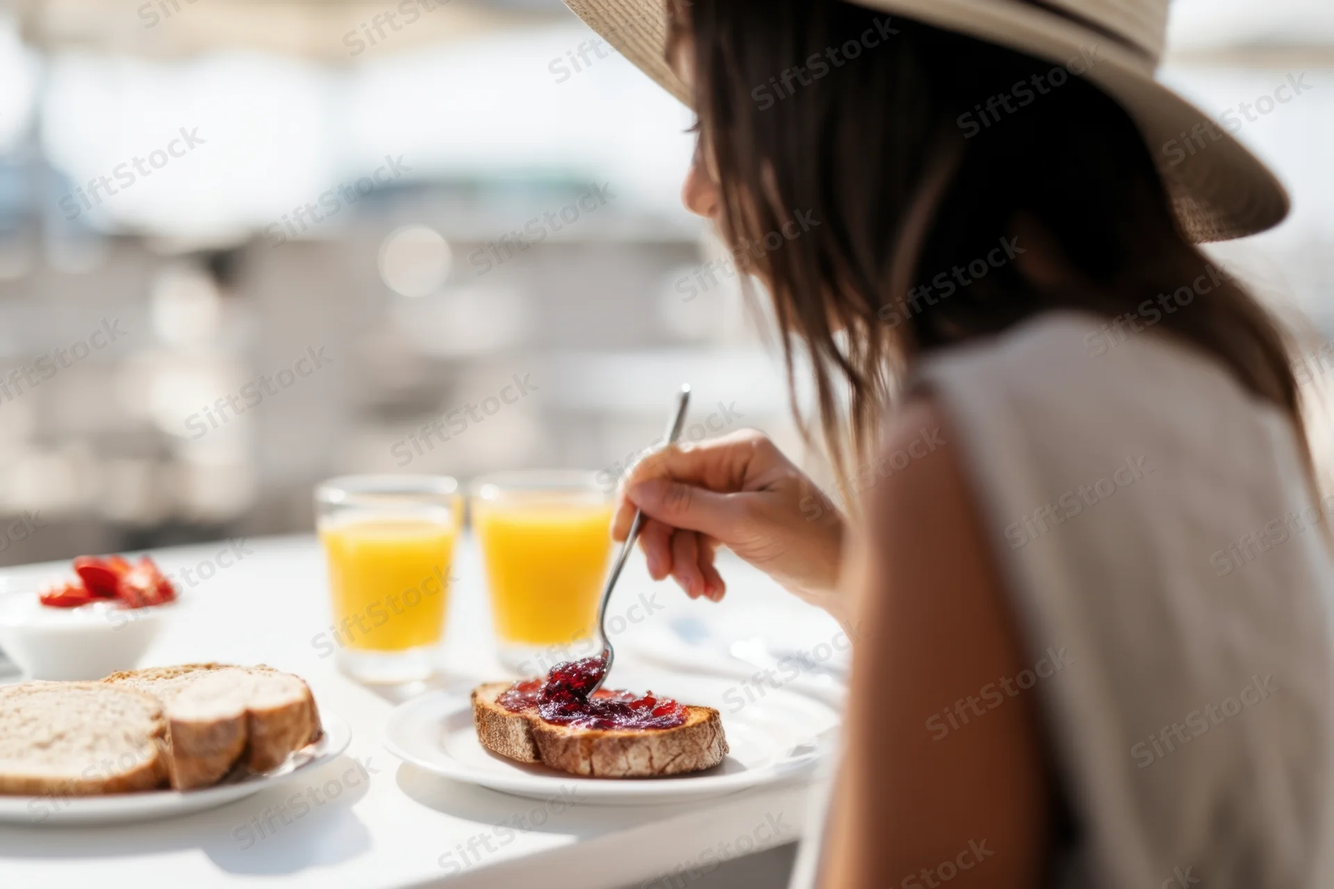 Woman spreading jam on toast at outdoor brunch table with orange juice and bread