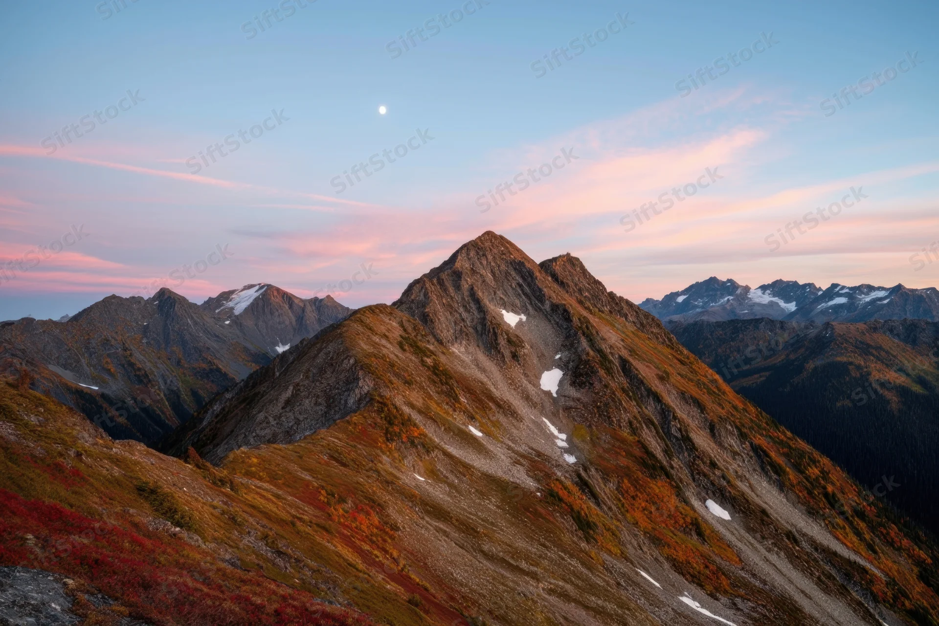 Jagged mountain peak at sunset with autumn foliage and snow patches in alpine landscape