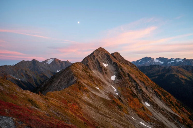 Jagged mountain peak at sunset with autumn foliage and snow patches in alpine landscape