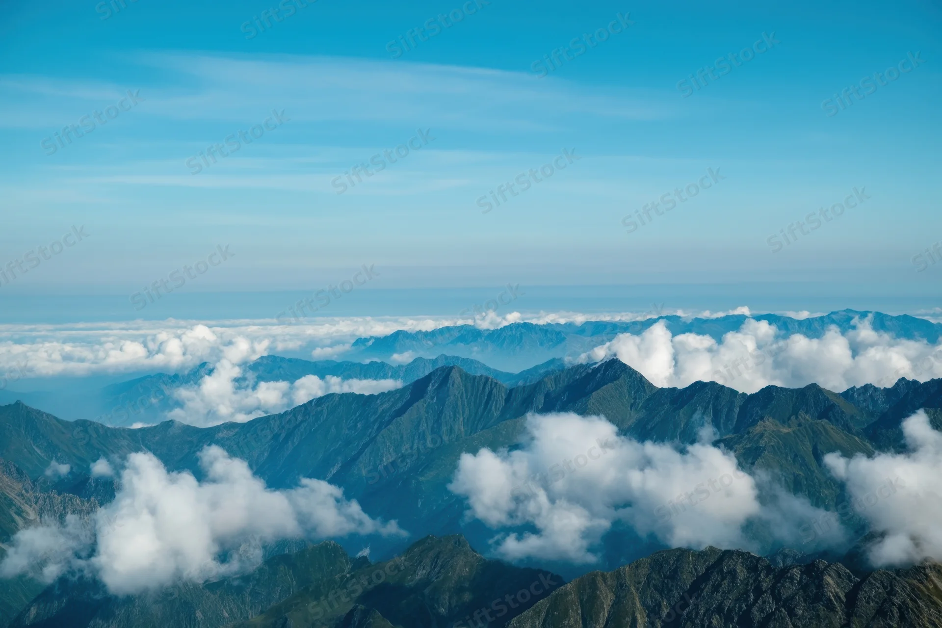 Panoramic view of rugged mountain peaks rising above clouds under a clear blue sky