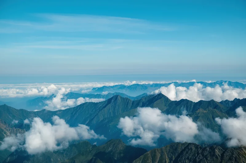 Panoramic view of rugged mountain peaks rising above clouds under a clear blue sky