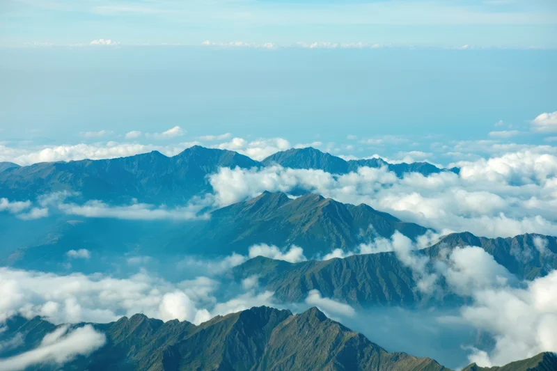 Aerial view of rugged mountain peaks rising above clouds in a panoramic landscape