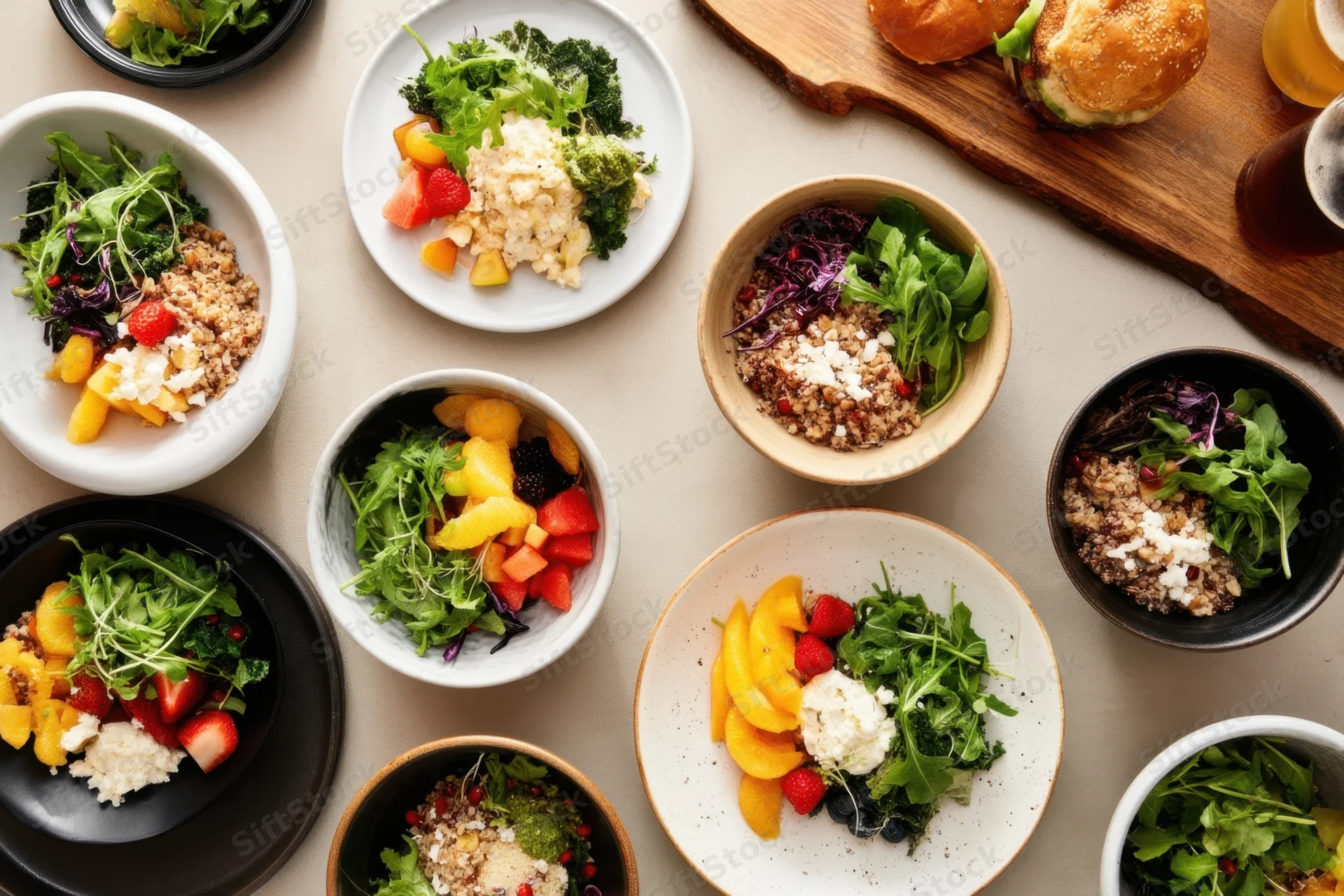 Colorful bowls of salad and fruit arranged on a table with sandwiches and beer in the background