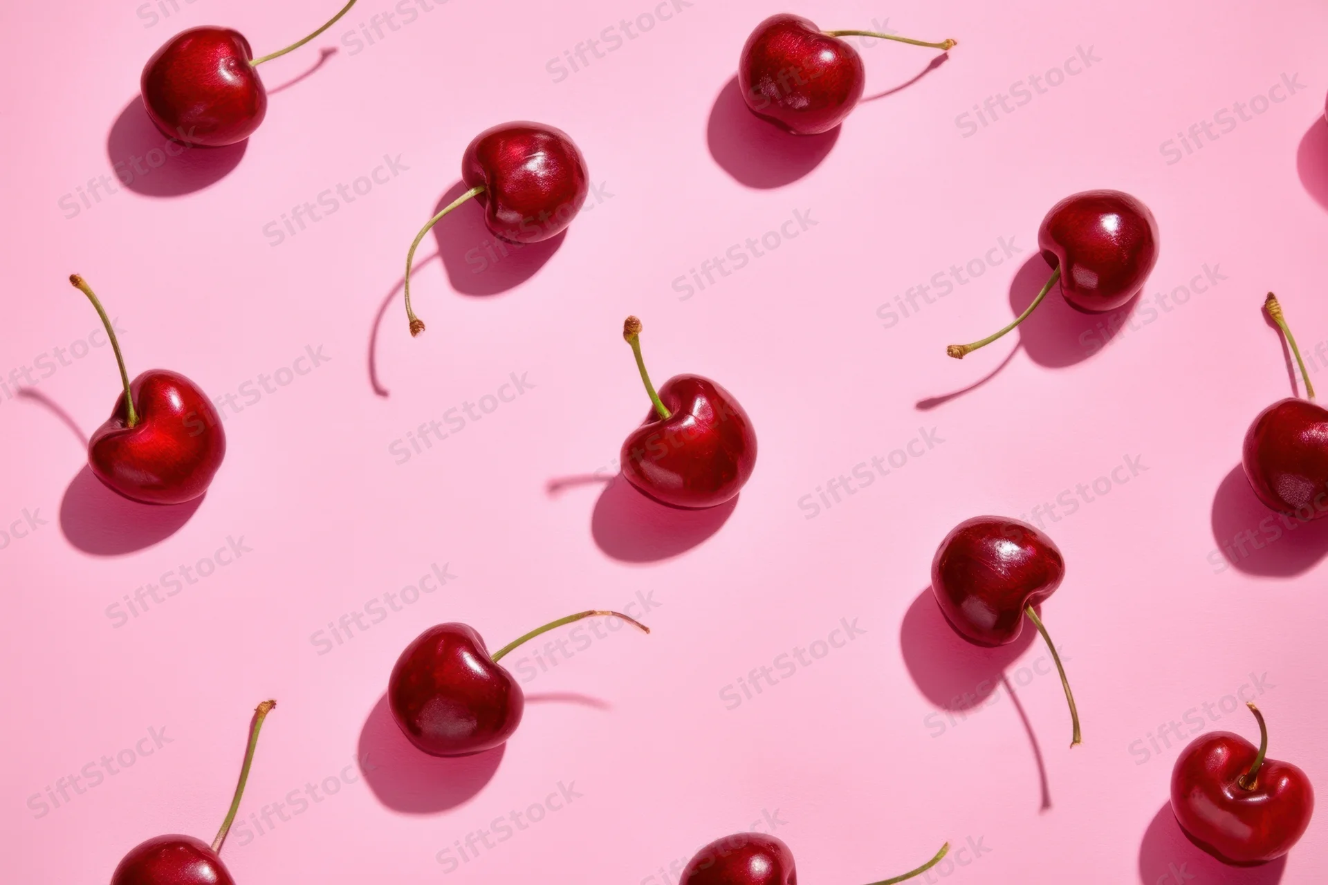 Glossy red cherries scattered across a pink surface in a flat lay still life arrangement