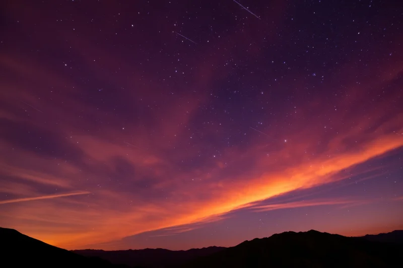 Starry night sky with glowing nebula above mountain silhouette