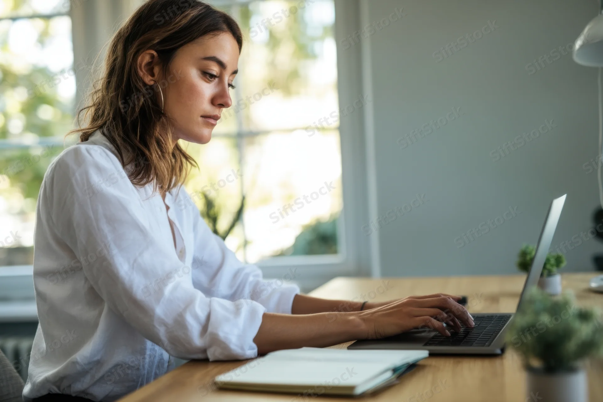 Woman typing on laptop at wooden desk by window in home office