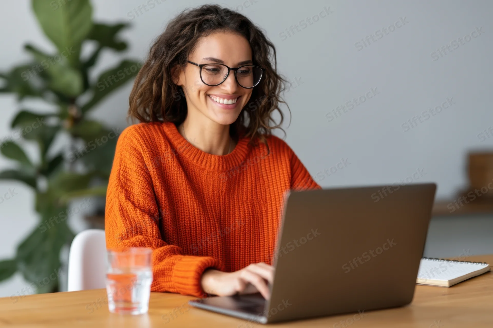 Woman typing on laptop at wooden desk smiling while working remotely