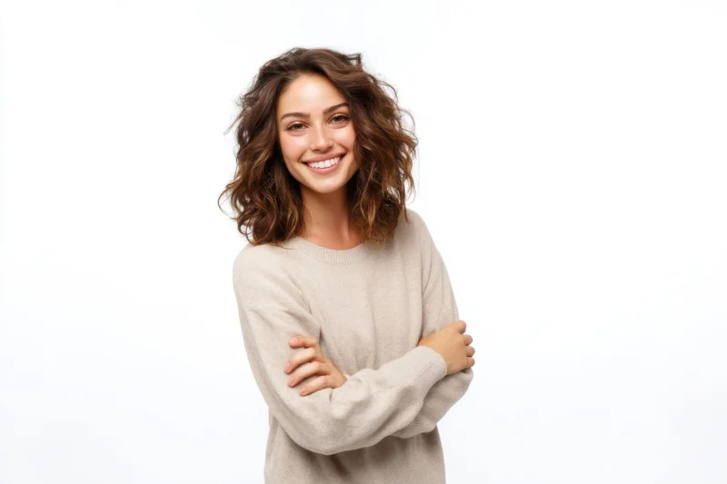 Woman smiling with arms crossed wearing beige sweater against white background