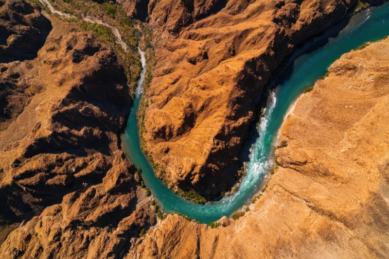 Aerial view of a winding turquoise river carving through a rugged orange canyon