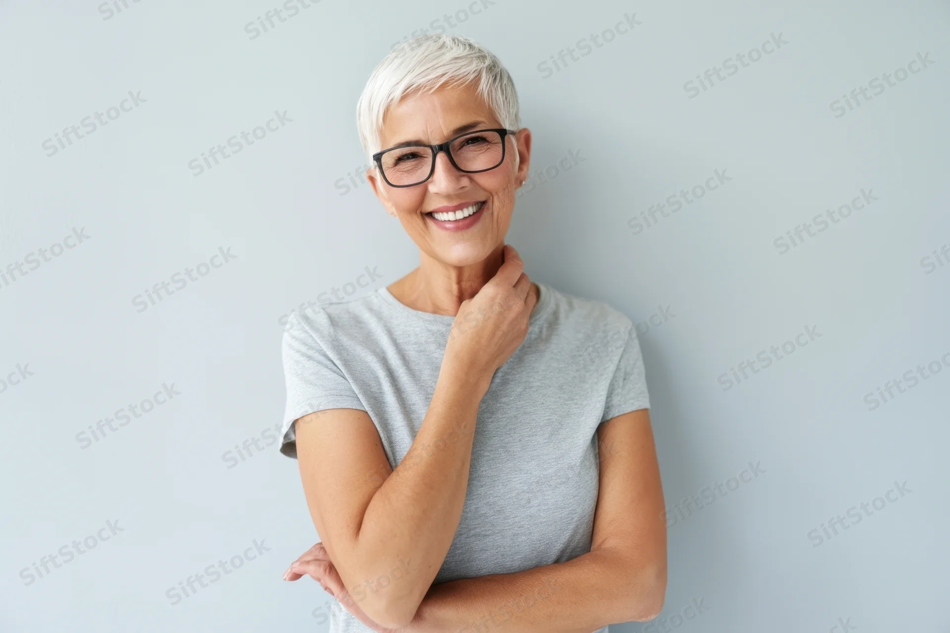 Smiling senior woman with short white hair and glasses posing in a gray tshirt against a light background
