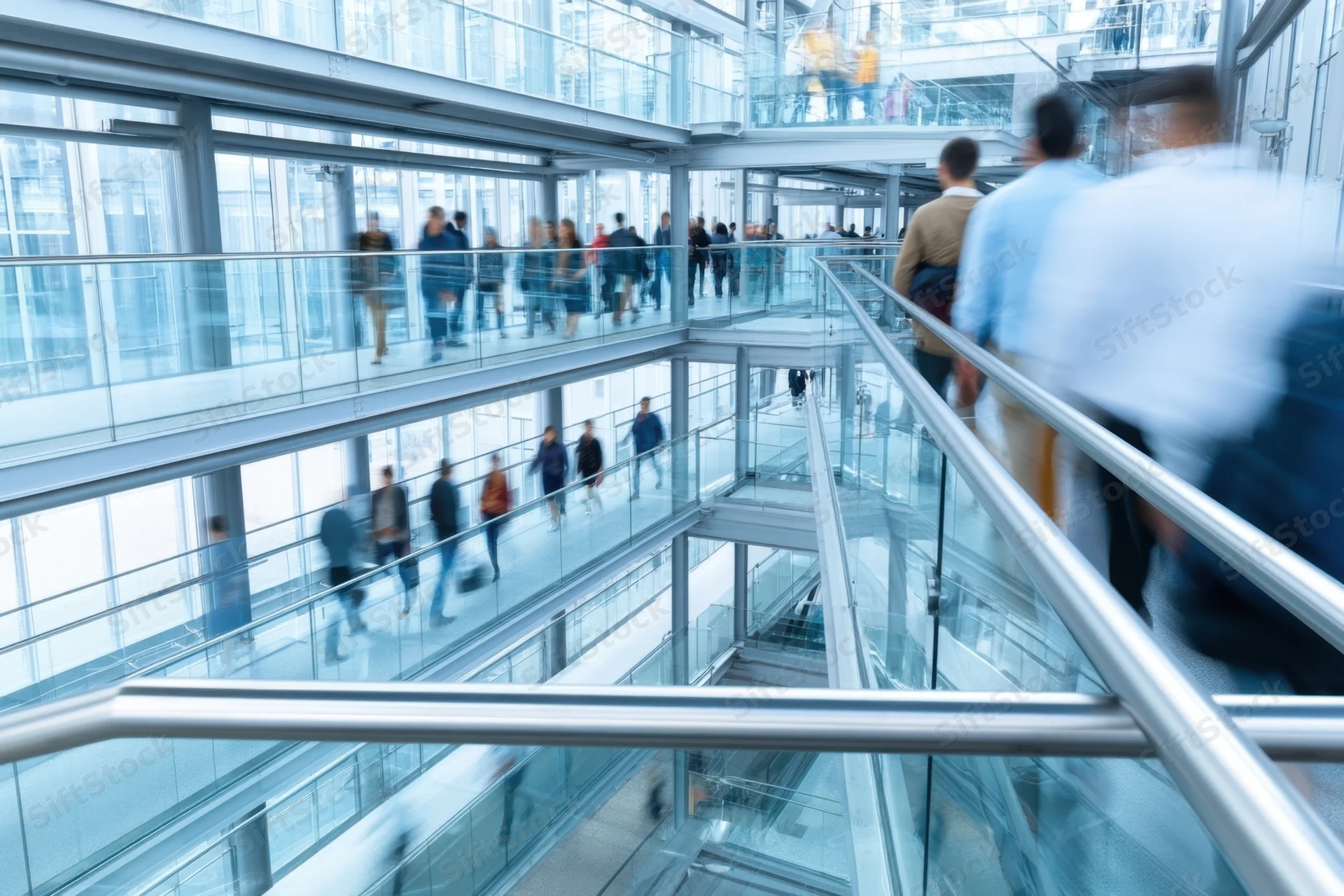 Motion-blurred people walking on multi-level glass walkways in a modern office building interior