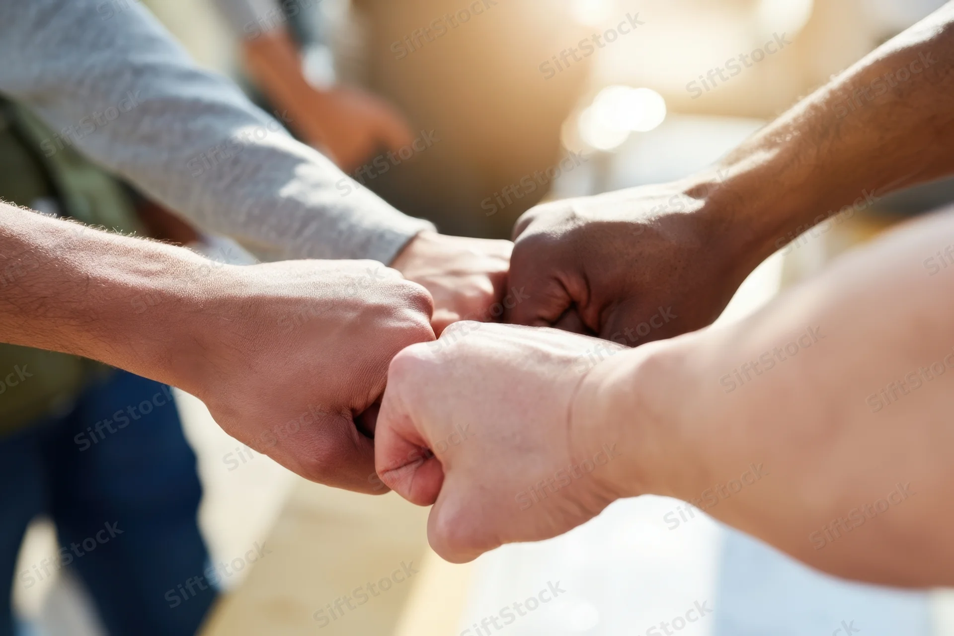 Multiple hands joining in a fist bump gesture outdoors in sunlight