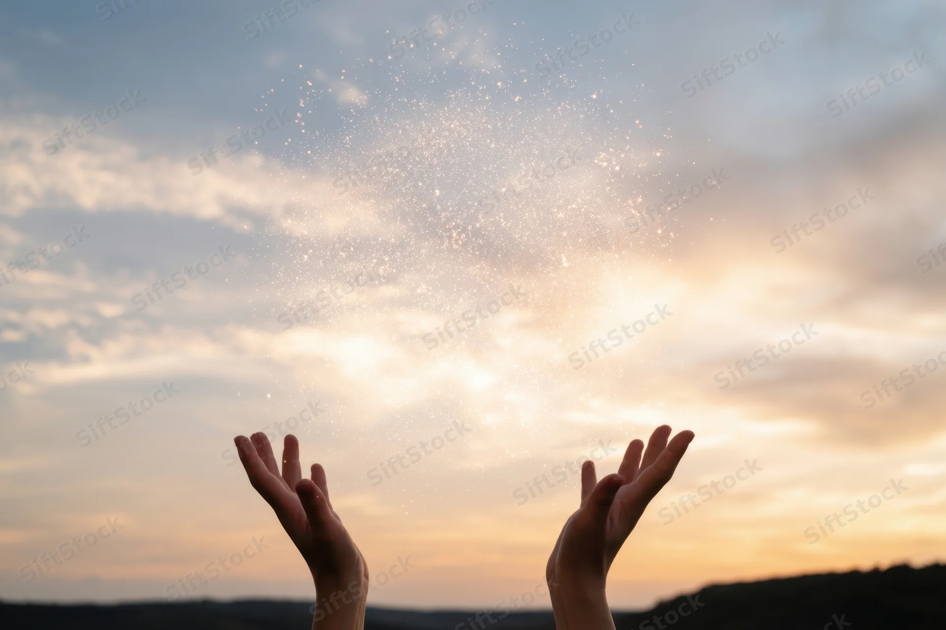 Hands raised toward glowing particles in the sky at sunset