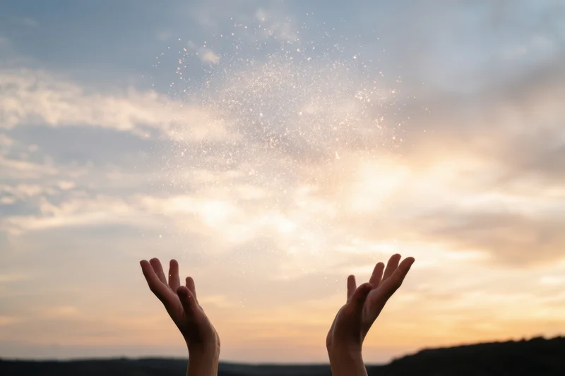 Hands raised toward glowing particles in the sky at sunset