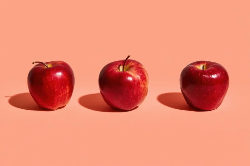 Three red apples arranged in a row on a peach-colored background