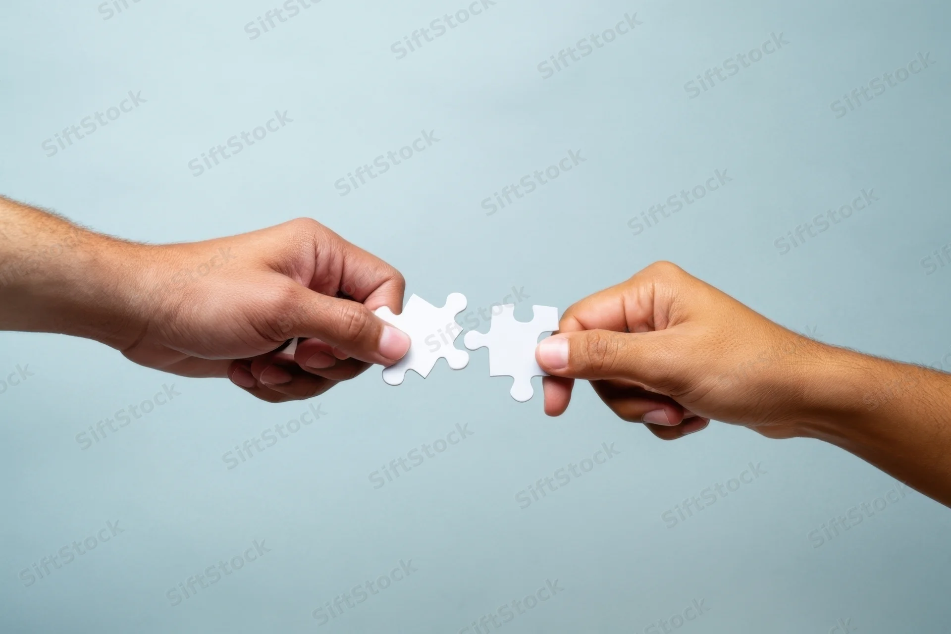 Two hands connecting white puzzle pieces against a soft blue background