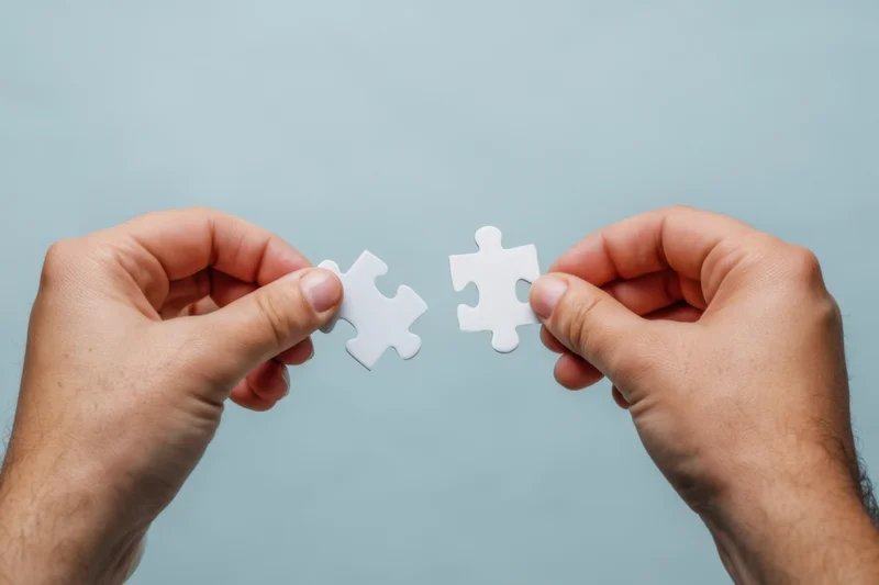 Two hands holding white puzzle pieces about to connect against a blue background