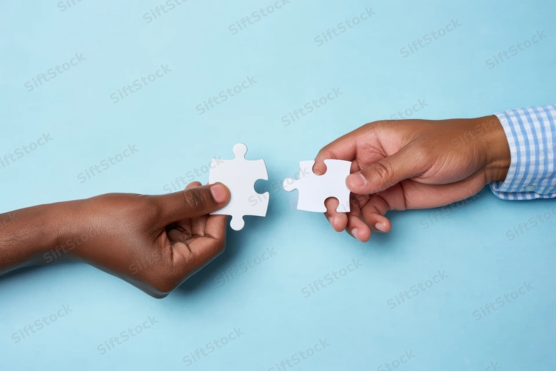 Two hands holding puzzle pieces facing each other on a light blue surface