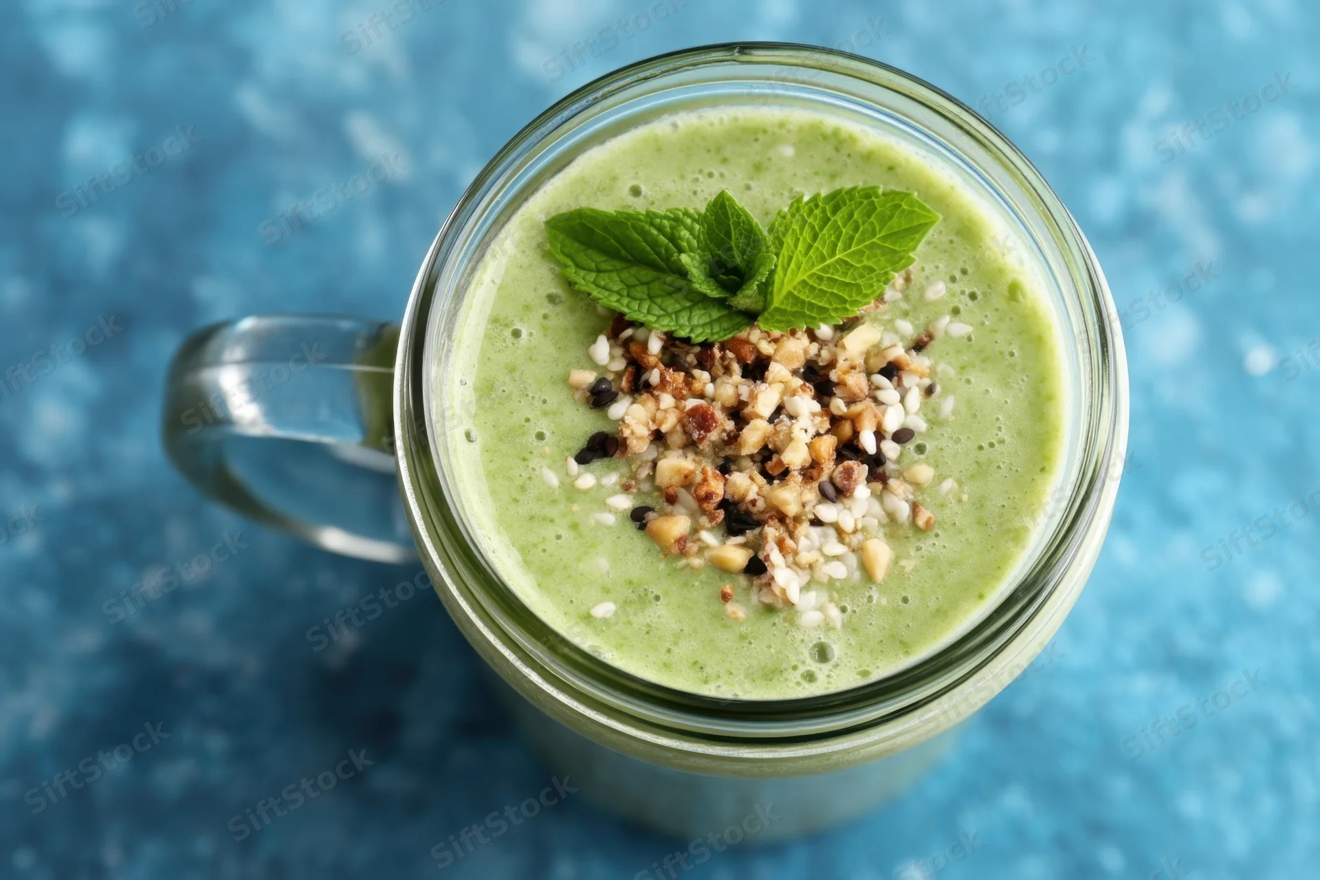 Green smoothie in a glass mason jar topped with mint and seeds on a blue surface
