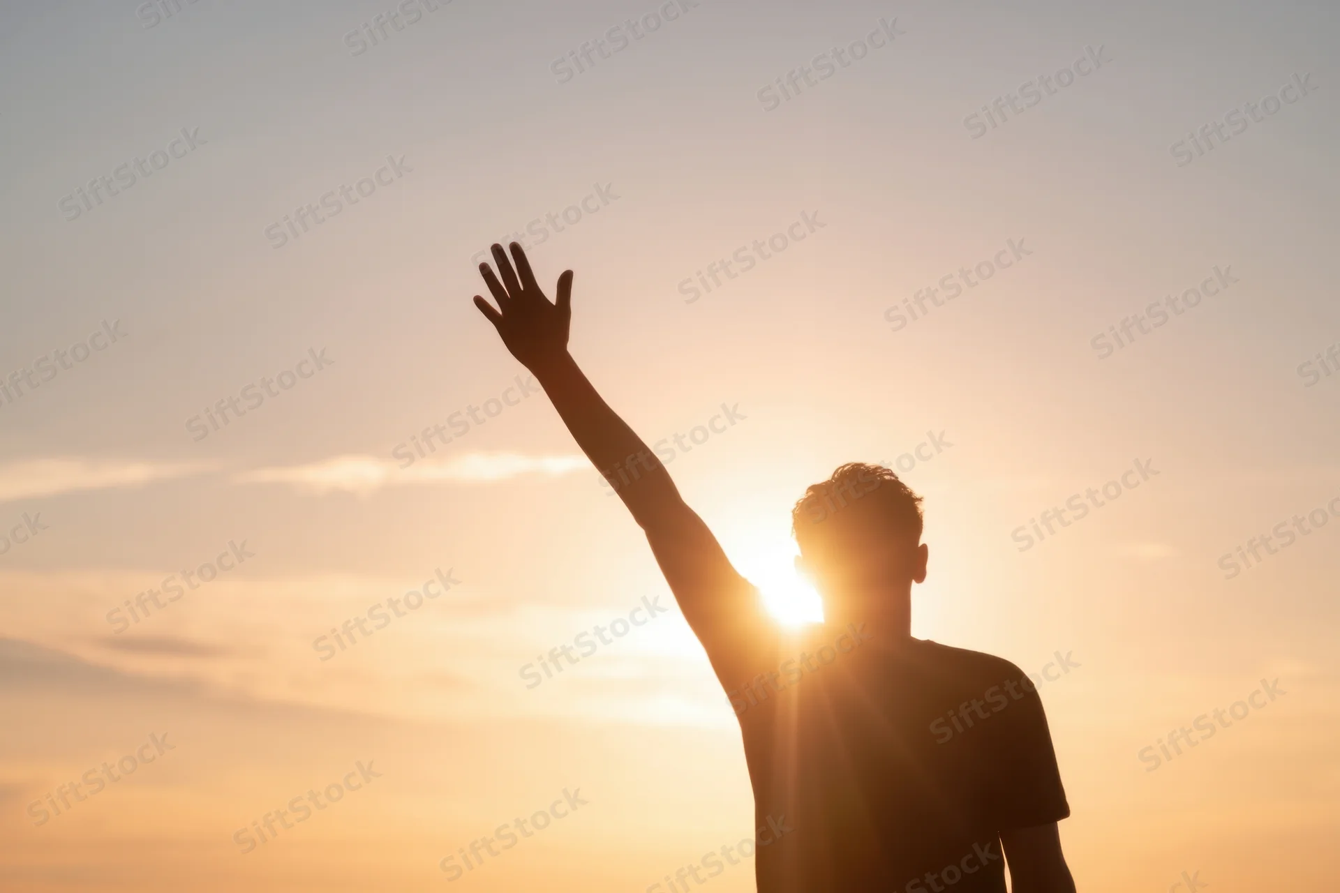 Silhouette of a young man raising his arm against a glowing sunset sky