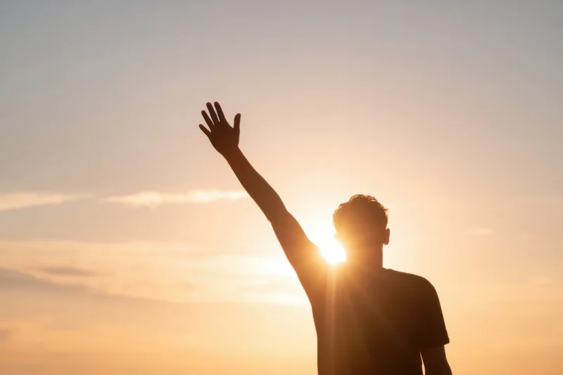Silhouette of a young man raising his arm against a glowing sunset sky