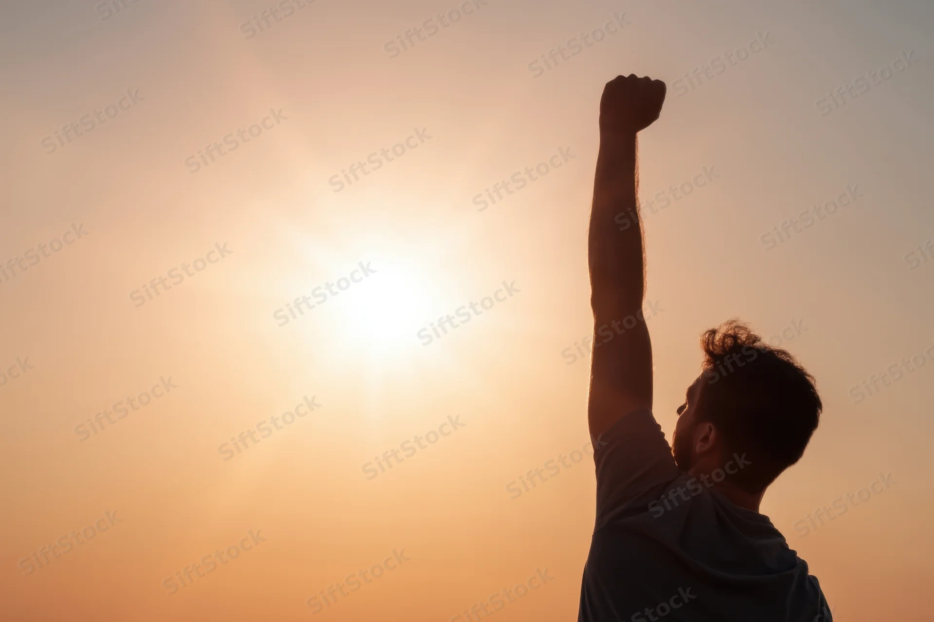 Man raising fist in silhouette against sunset sky