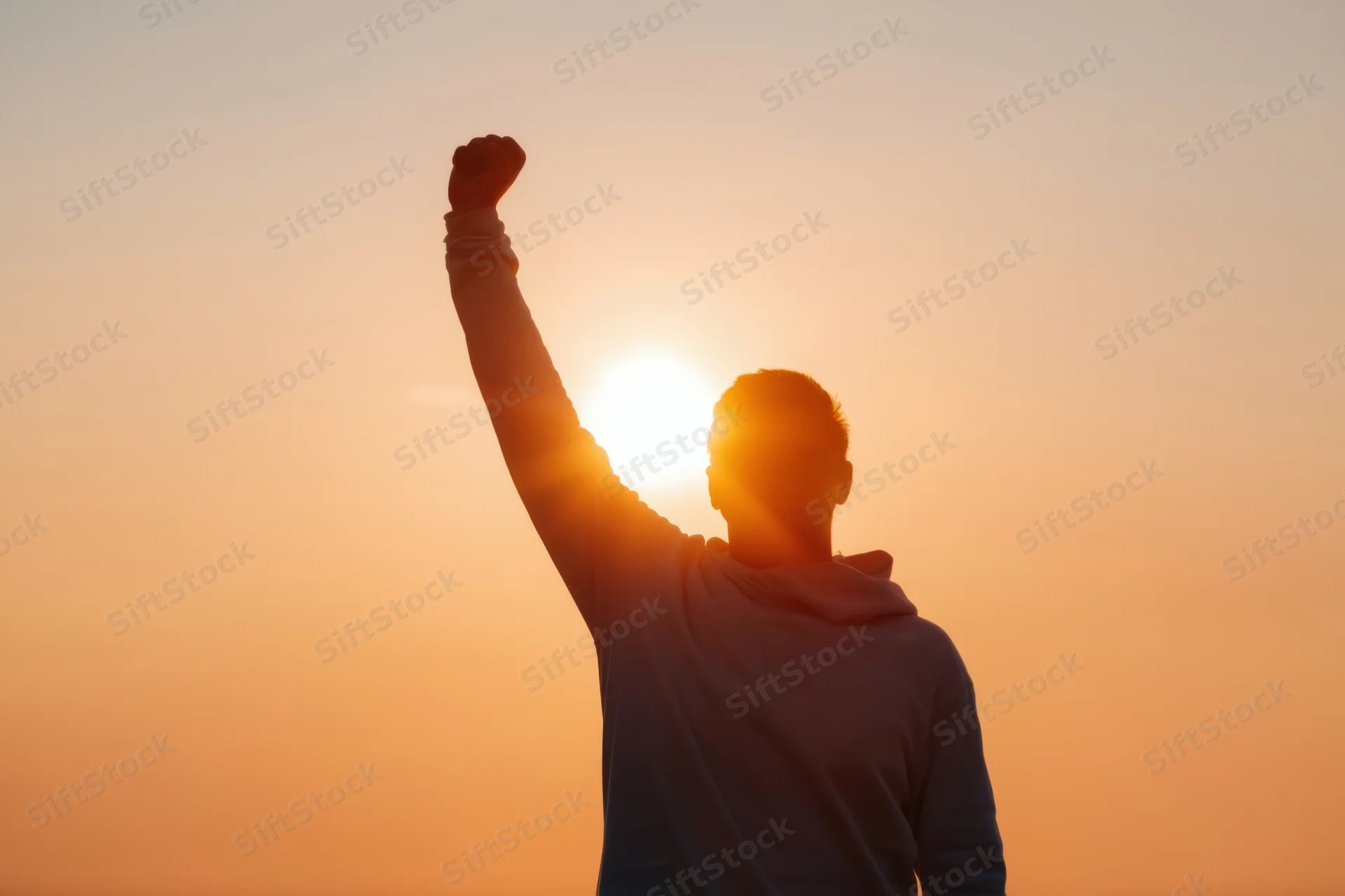 Silhouette of a man raising his fist in triumph against a sunset sky
