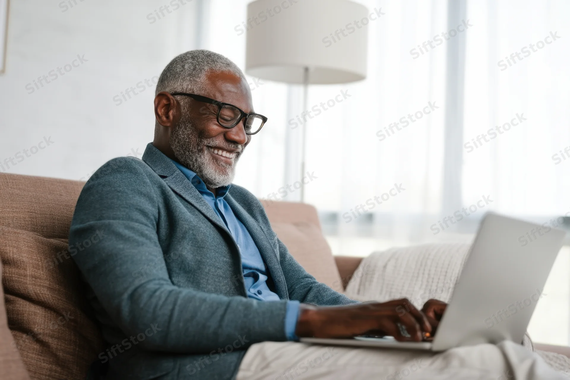 Smiling senior man typing on laptop while sitting on couch in living room