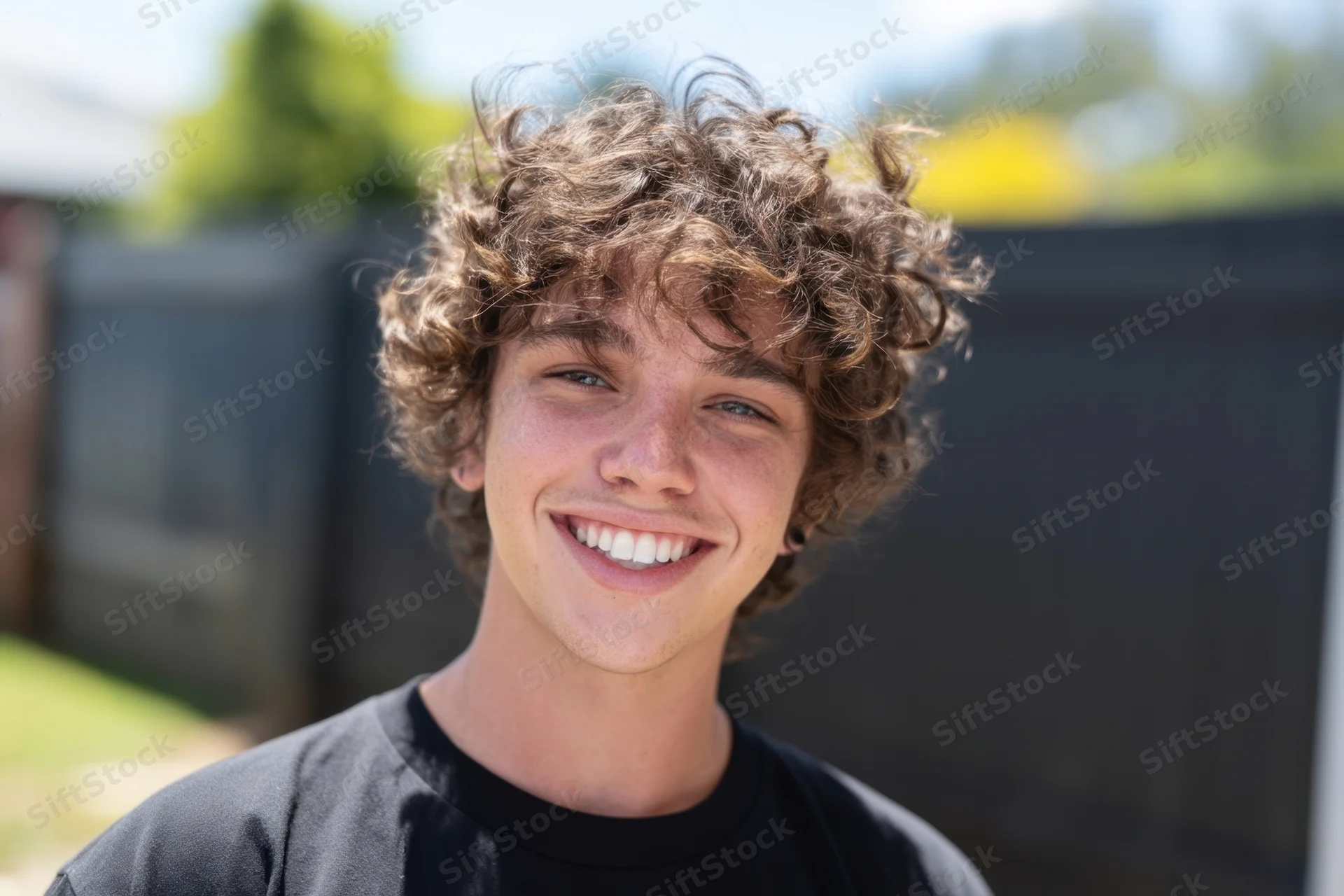 Smiling young man with curly brown hair wearing a black t-shirt outdoors