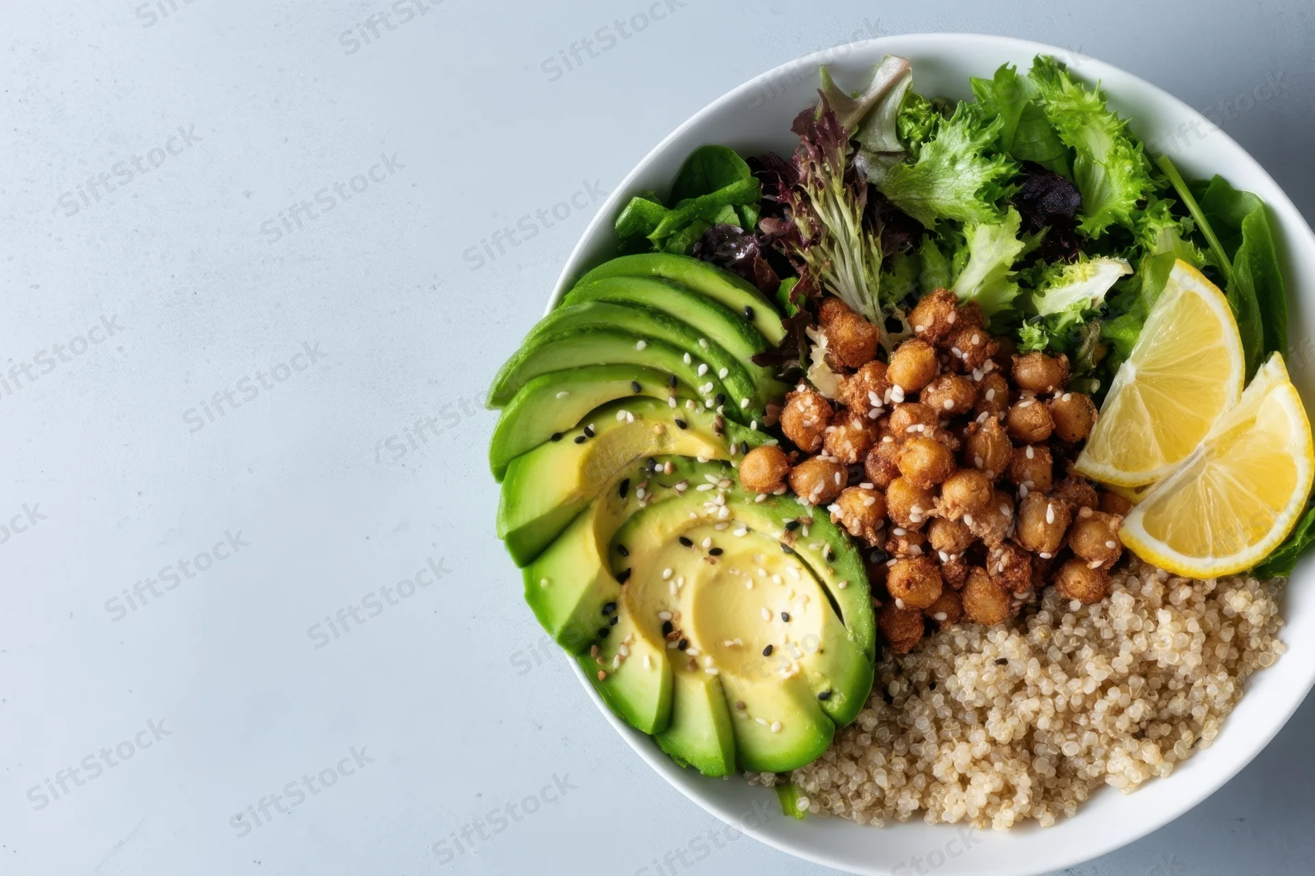 A salad bowl with avocado slices, quinoa, chickpeas and lemon on a white countertop