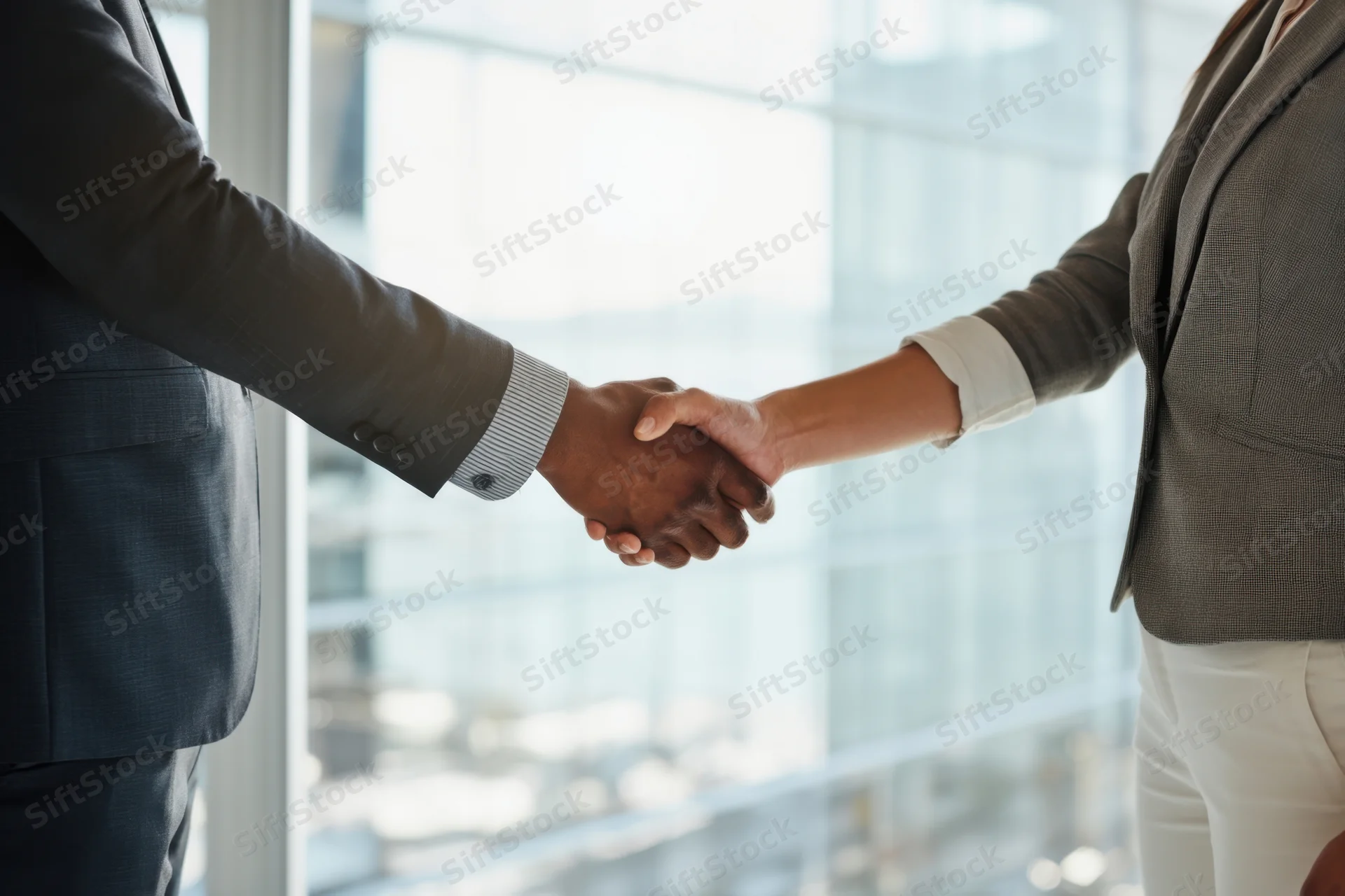 Two professionals shaking hands in a modern office with a city view through a large window