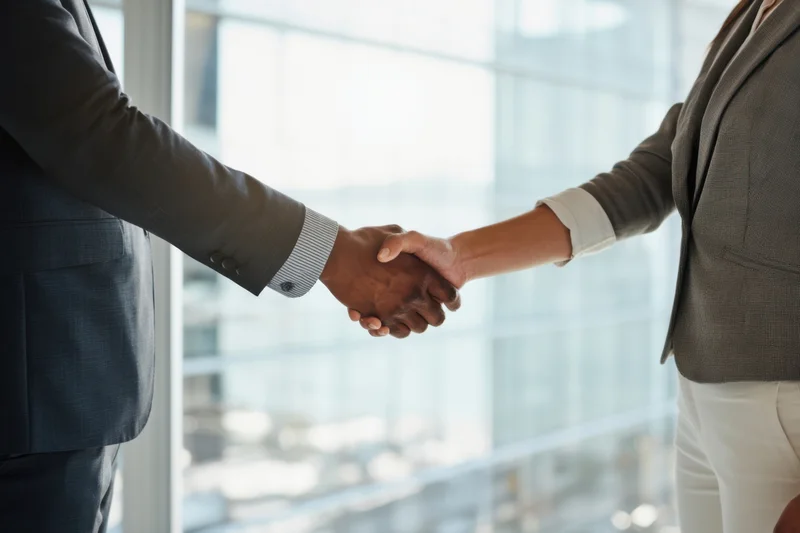 Two professionals shaking hands in a modern office with a city view through a large window