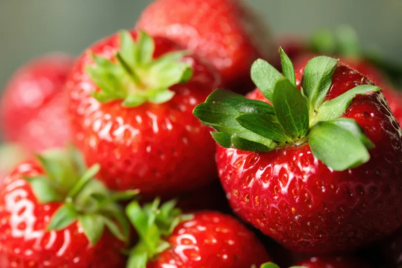 Close-up of ripe strawberries with glossy red surface and green leaves clustered together