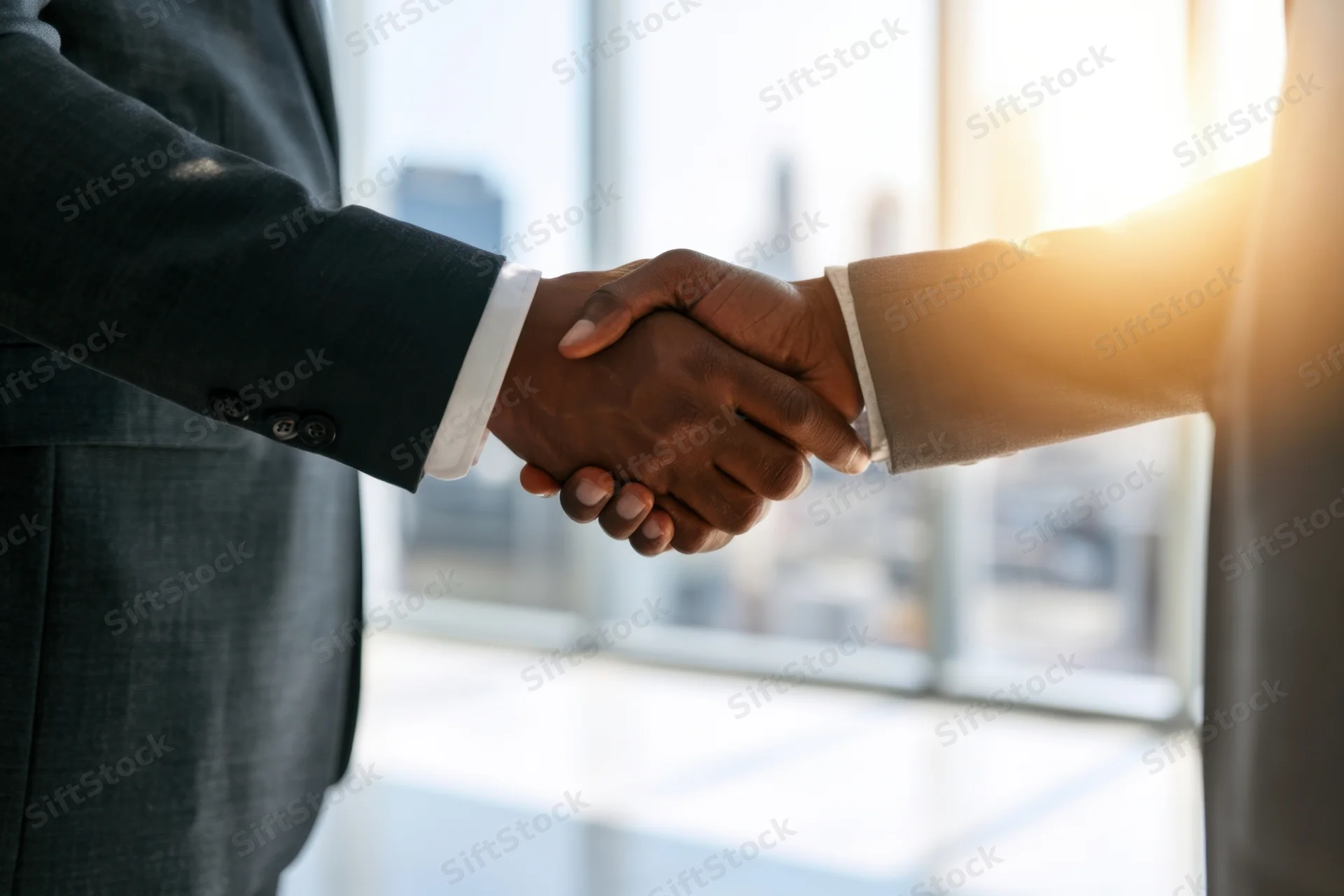 Two business professionals shaking hands in an office with city view through window
