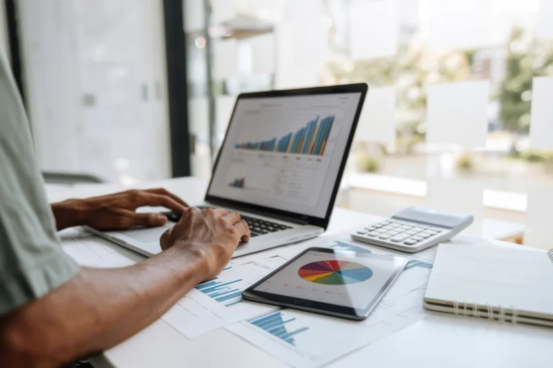 Man analyzing financial data on laptop and tablet at office desk
