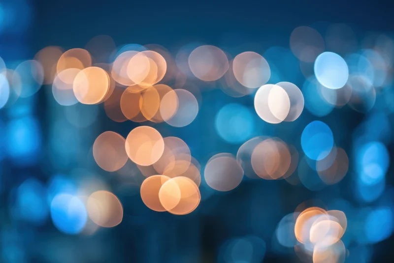 Blurred city lights at night with warm and cool bokeh circles against a dark blue background