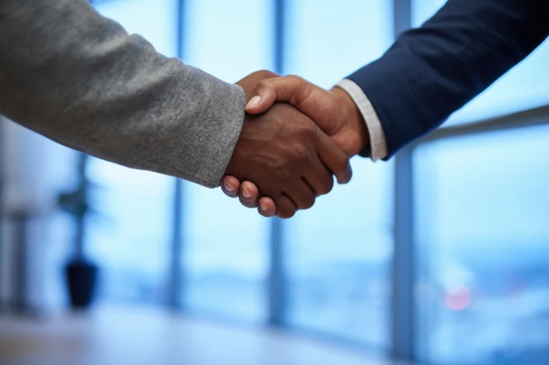Close-up of two business professionals shaking hands in a modern office with city view through glass windows