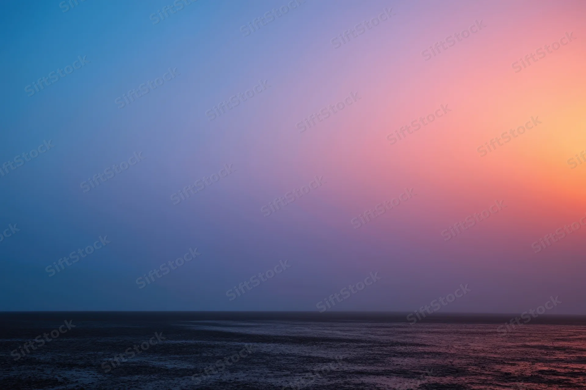 Twilight sky over calm ocean with blue and pink gradient at horizon