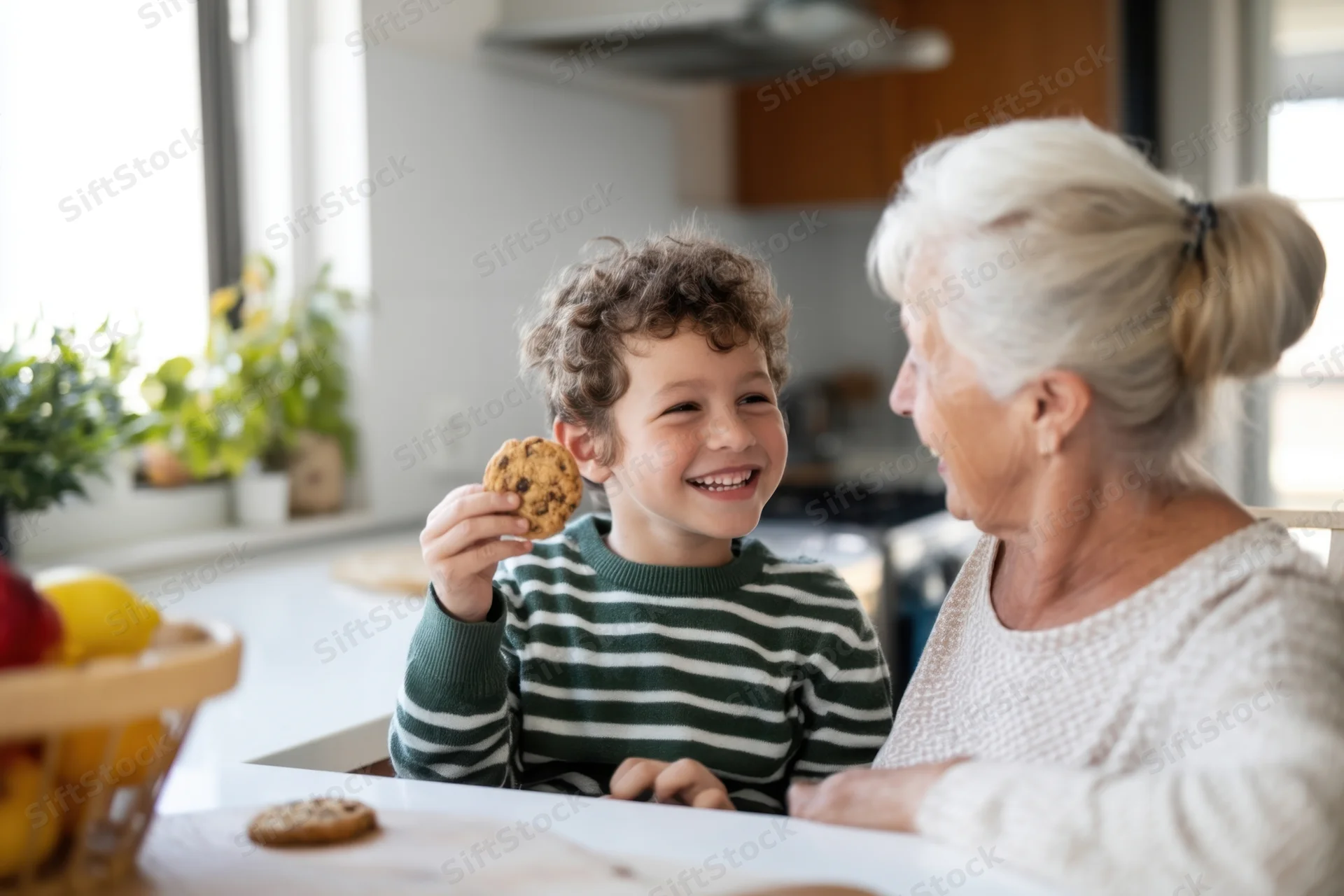 Grandson holding a cookie and smiling at his grandmother in a sunlit kitchen